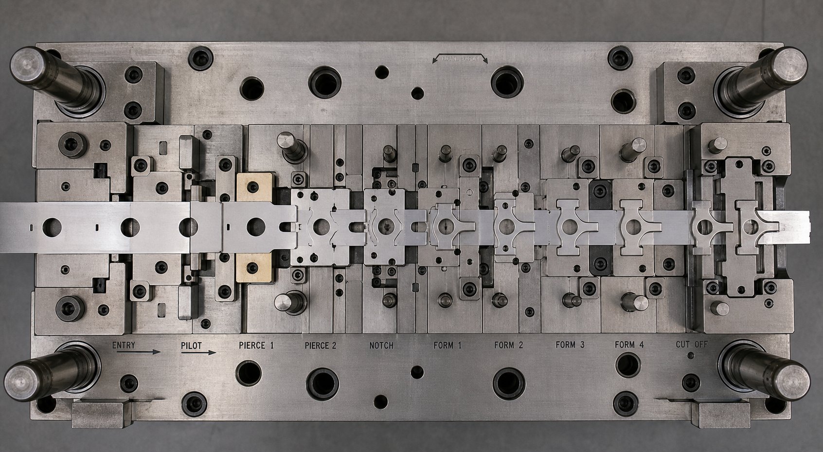 a progressive die strip layout showing multiple stations where parts are gradually shaped while remaining connected to the carrier strip